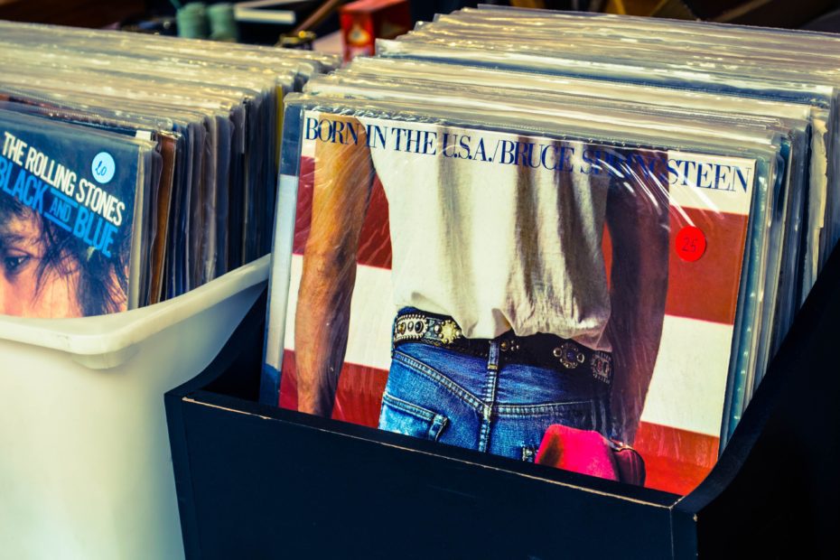 Two collections of records in storage containers at a vinyl record store. At the front of the left collection you can see The Rolling Stones album "Black and Blue". On the right, you can see Bruce Springsteen's album "Born in the U.S.A"