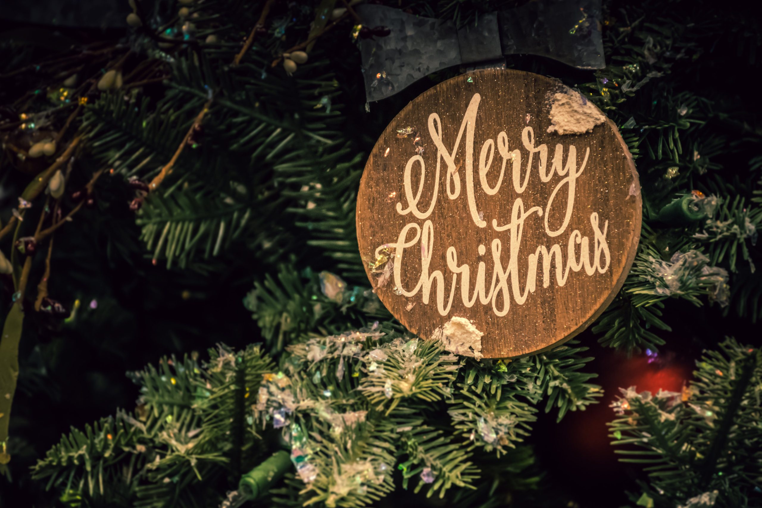 An ornament in a Christmas tree that says "Merry Christmas" in a fancy cursive font.